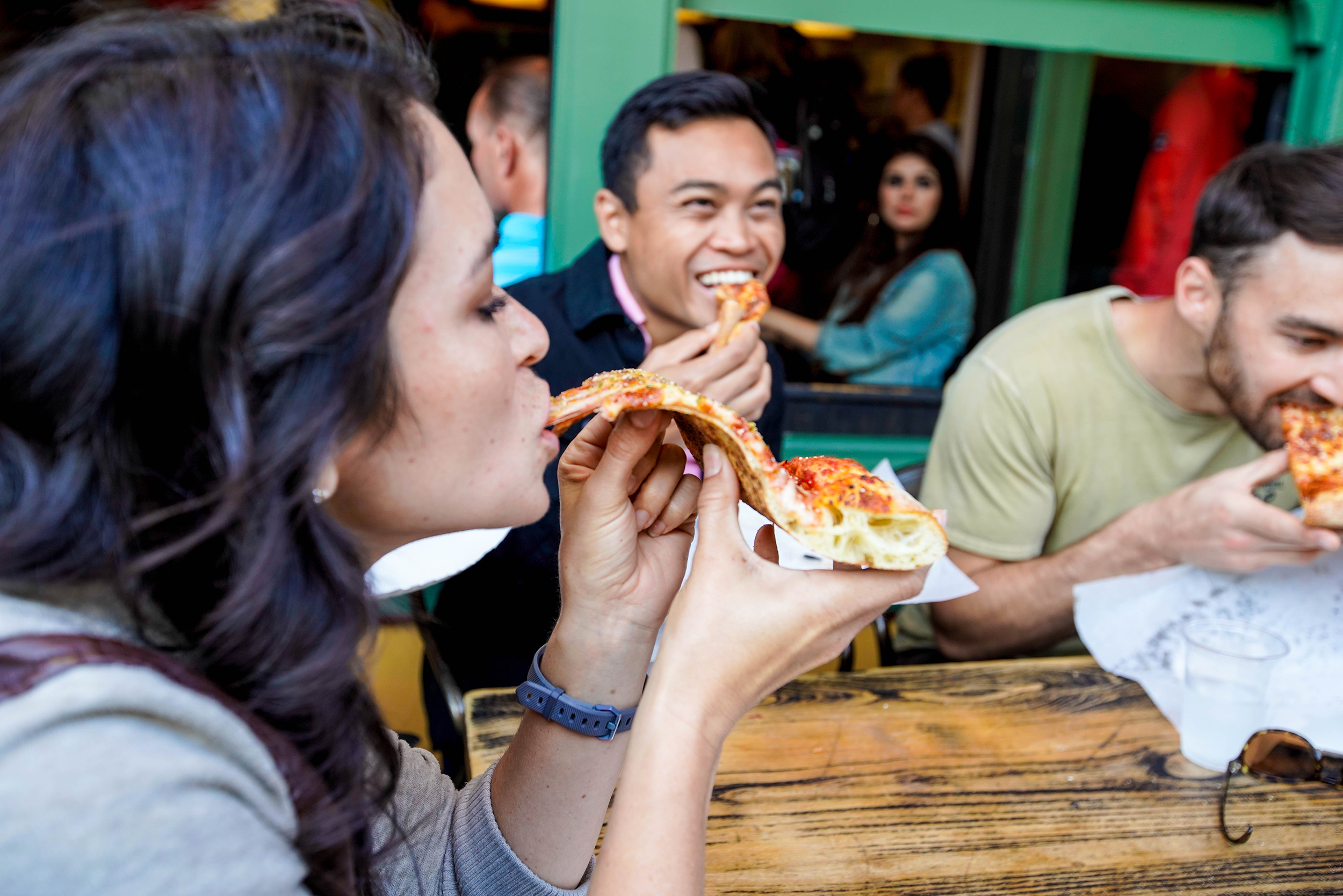 Pizza pub tour: guests biting into slices of New York–style pizza at an outdoor pub table in San Francisco.