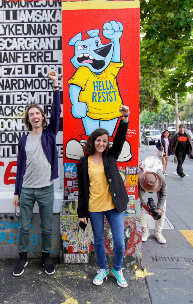 Team building San Francisco: Two team members cheering in front of a “Hella Resist” street mural during a private group food tour in San Francisco.